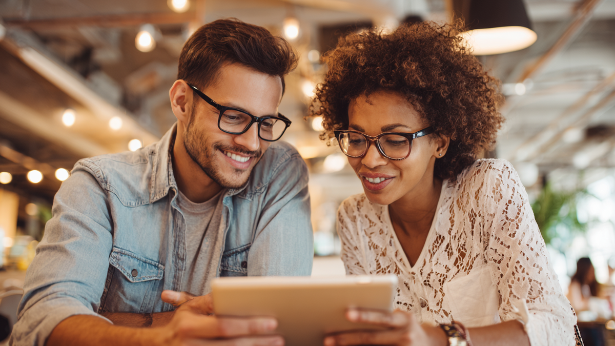 Paar in Café blickt lächelnd gemeinsam auf Tablet und plant ihre Finanzen mit Gemeinschaftskonto
