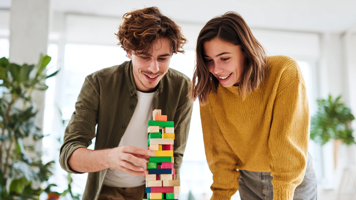 Ein junger Mann und eine junge Frau stehen an einem Tisch und bauen einen Turm aus Bausteinen