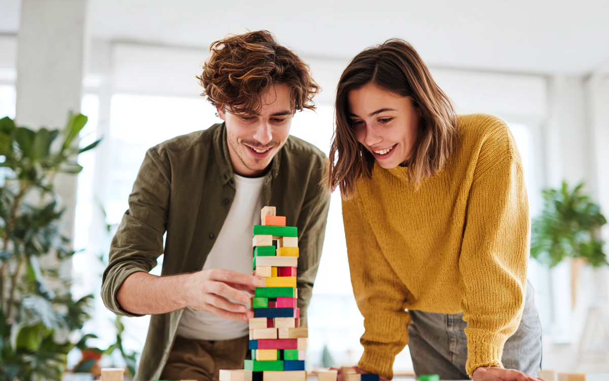 Ein junger Mann und eine junge Frau stehen an einem Tisch und bauen einen Turm aus Bausteinen